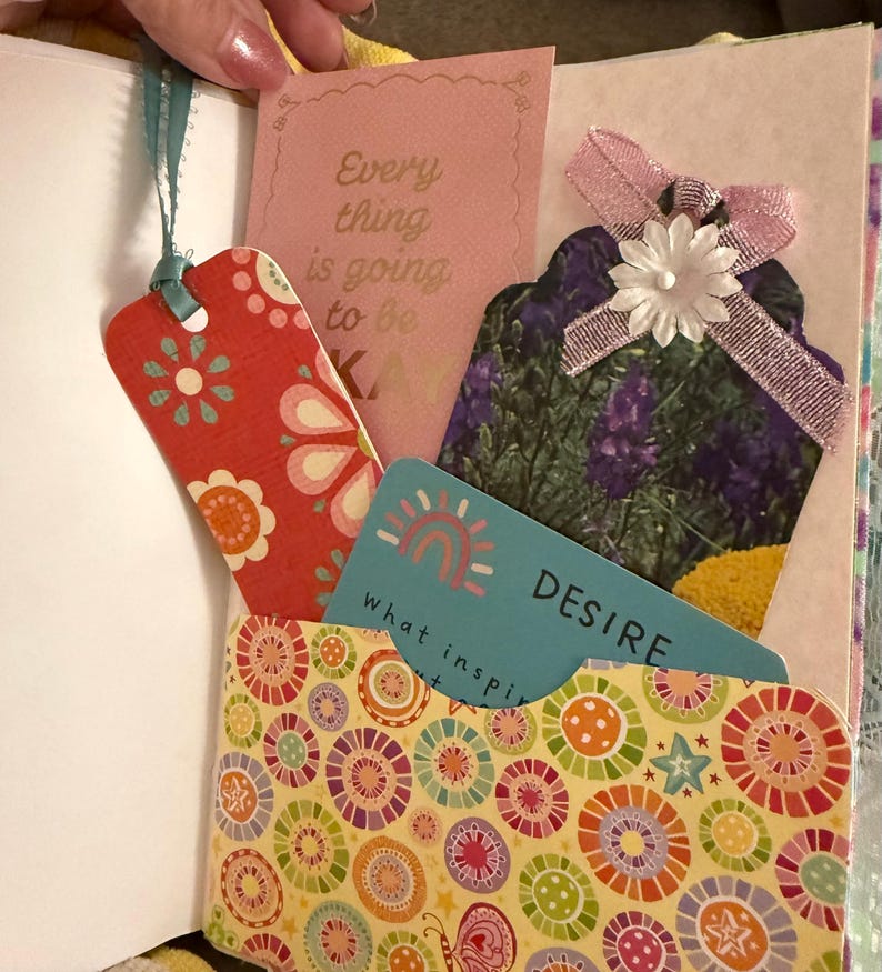 May include: A yellow pocket with a colorful circular pattern. The pocket contains a blue card with a rainbow and the text "what inspires you" and "DESIRE". There is also a pink card with the text "Every thing is going to be okay" and a red bookmark with a floral pattern.