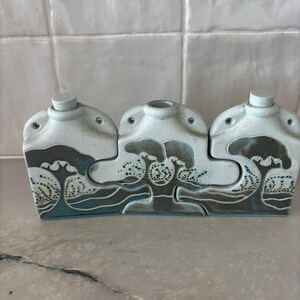 May include: A ceramic, three-part container with a light blue and gray color scheme. Each section features a stylized tree design with blue and yellow accents. The container has a lid on two of the sections.