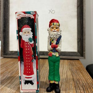 Op de afbeelding: Een Hermitage Pottery Santa Claus beeldje in een rode jas, groene broek en zwarte laarzen staat naast een doos met een soortgelijk Santa Claus beeldje. Op de doos staat de tekst "Hermitage Pottery" en "1995 Limited Edition".
