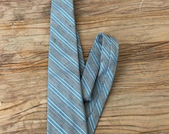 May include: A gray necktie with light blue stripes. The tie is made of a textured fabric and is lying on a wooden surface. The tie is folded over itself.