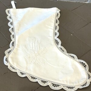 May include: White Christmas stocking with a lace trim and an embroidered design of a poinsettia and candles.