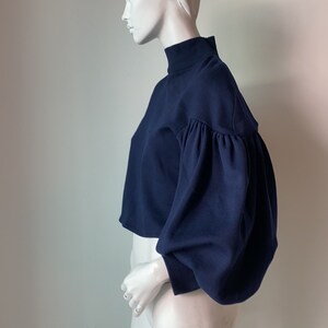 K&ouml;nnte beinhalten: Ein dunkelblauer, kurzer Pullover mit hohem Kragen und langen, bauschigen &Auml;rmeln.