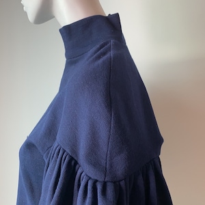 K&ouml;nnte beinhalten: Ein dunkelblauer, kurzer Pullover mit Puff&auml;rmeln. Der Pullover hat einen hohen Kragen und eine figurbetonte Silhouette.