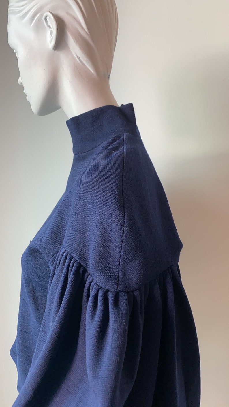 K&ouml;nnte beinhalten: Ein dunkelblauer, kurzer Pullover mit Puff&auml;rmeln. Der Pullover hat einen hohen Kragen und eine figurbetonte Silhouette.