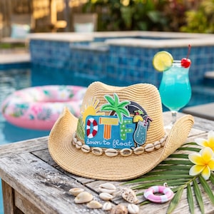 May include: A tan straw cowboy hat featuring a band of small white seashells and a large colorful patch on the front. The patch displays a yellow sun, a green palm tree, and a blue cocktail with the text DTF and down to float written below.