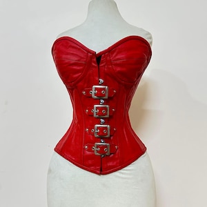 Um espartilho de couro vermelho com decote coração e quatro fivelas prateadas.