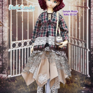 May include: A doll wearing a plaid shirt with lace trim, a beige skirt with lace overlay, and white lace-up boots. The doll has long, dark red hair and blue eyes. The doll is standing in front of a metal gate with a sign that reads "Doll-Candy www.doll-candy.com". The sign also says "Sample Model: Volks SD Girl".