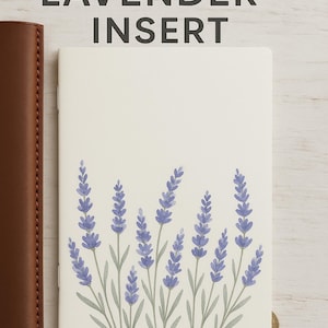 Puede incluir: Un inserto de lavanda imprimible con un diseño de acuarela. El inserto presenta un fondo crema con un diseño floral de lavanda en la parte inferior. El texto "PRINTABLE LAVENDER INSERT" está en la parte superior. Un cuaderno de cuero marrón está a la izquierda.