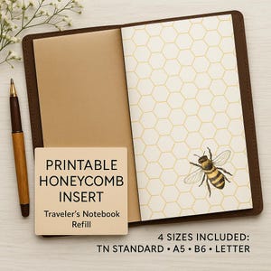 Op de afbeelding: Open bruin leren reizigersnotitieboek met een honingraatpatroon inlegvel en een bijenillustratie. Een vierkante kaart leest "PRINTABLE HONEYCOMB INSERT Traveler's Notebook Refill". Inclusief TN Standard, A5, B6 en Letter formaten. Een pen ligt ernaast.