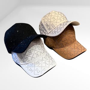 Puede incluir: Tres gorras de béisbol con un patrón de diamante y diamantes de imitación. Las gorras son negras, blancas y marrones.