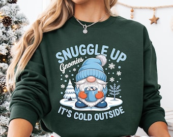 May include: A dark green sweatshirt with the text "Snuggle Up Gnomies, It's Cold Outside" and a graphic of a gnome holding a mug. The gnome is wearing a blue hat and holding a blue mug. The person is wearing red and white plaid pajama pants and holding a mug with a Santa Claus graphic.