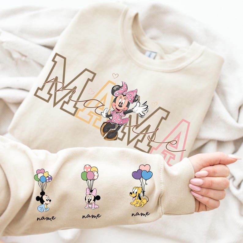 May include: Cream-colored sweatshirt featuring the word "MAMA" in brown, peach, and pink lettering, with a Minnie Mouse graphic. The sleeve displays three cartoon characters with balloons, each with a "name" label.