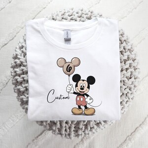 May include: A white ceramic mug with a black handle and the text "But First, Coffee" in a bold, black font. The mug is set against a blurred background, suggesting a cosy setting.