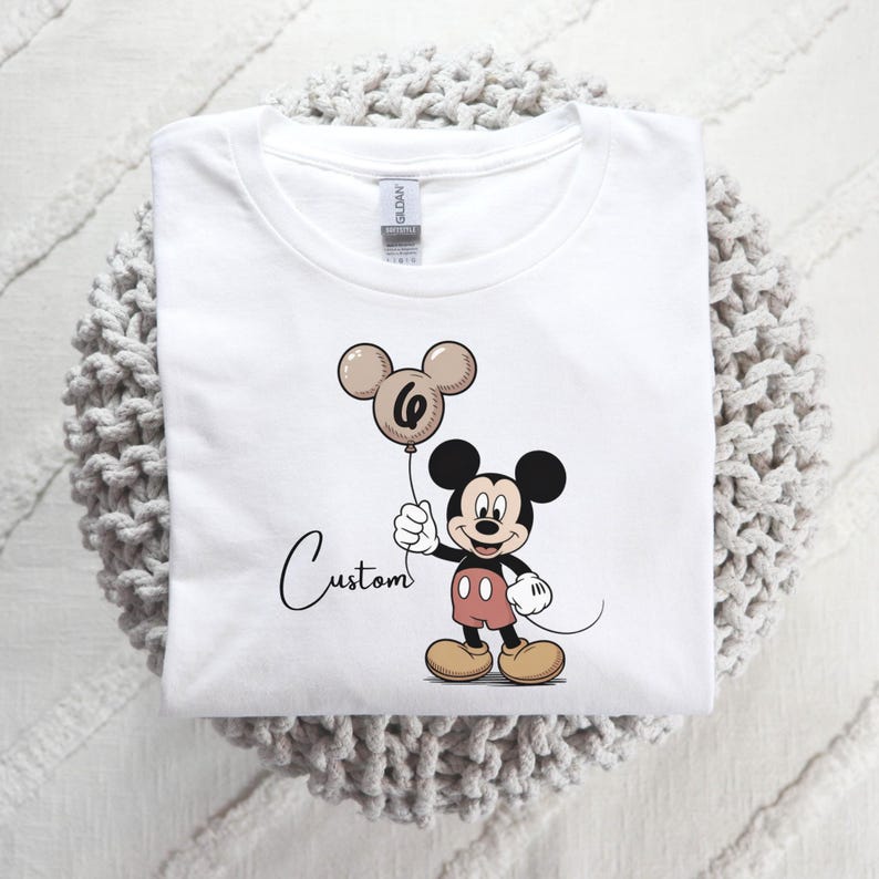 May include: A white ceramic mug with a black handle and the text "But First, Coffee" in a bold, black font. The mug is set against a blurred background, suggesting a cosy setting.