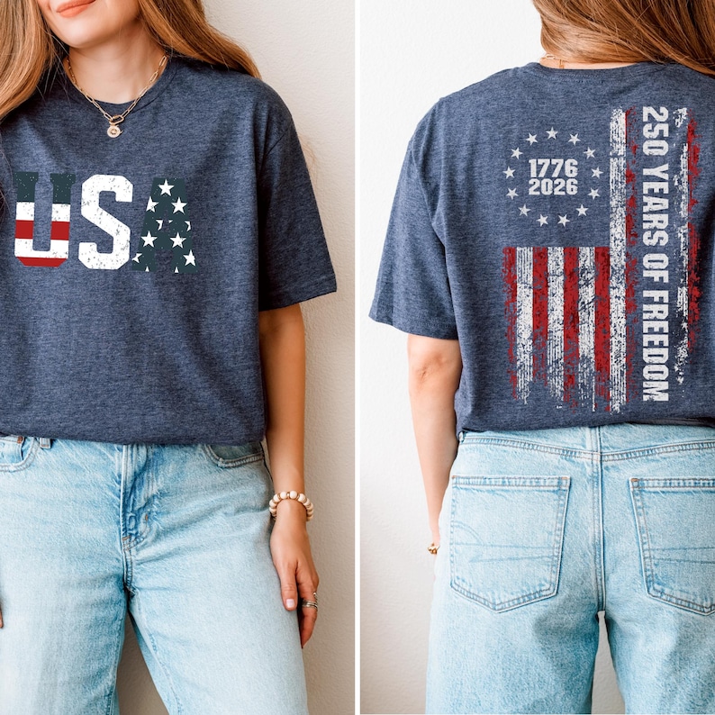 May include: A heather navy blue t-shirt featuring a distressed USA graphic on the front. The back displays a distressed American flag design with a circle of stars, the years 1776 and 2026, and the text 250 YEARS OF FREEDOM in white lettering.