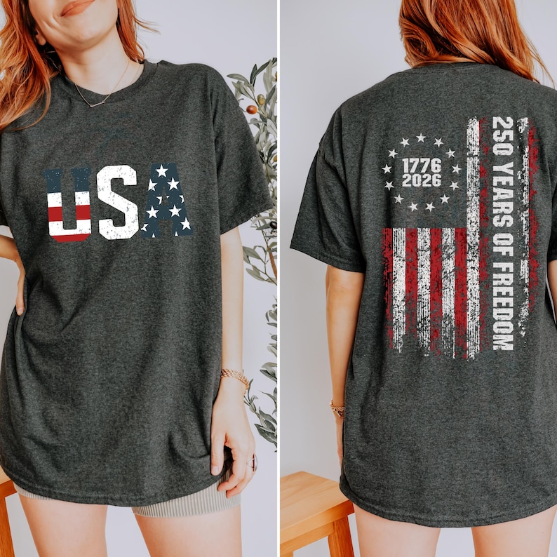 May include: A dark charcoal gray t-shirt featuring a distressed USA graphic on the front with red, white, and blue flag patterns. The back displays a distressed American flag design with a circle of stars, the years 1776-2026, and 250 YEARS OF FREEDOM.