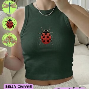 Könnte beinhalten: Ein dunkelgrünes, geripptes Racerback-Tanktop mit einem zentralen, gestickten Marienkäfer-Motiv mit rotem Panzer und schwarzen Punkten. Das Kleidungsstück hat einen hohen Ausschnitt und eine körpernahe Passform. Weitere Insektenmotive sind in Kreisen zu sehen.