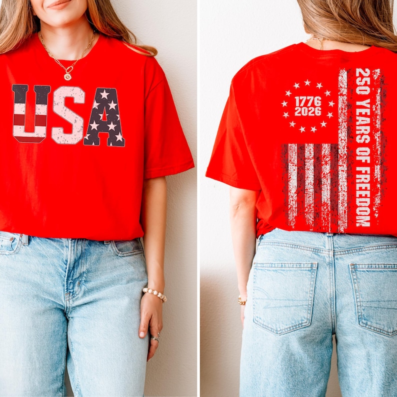 May include: A bright red short-sleeve t-shirt. The front features the text USA in a distressed flag pattern. The back displays a circular arrangement of stars above the years 1776 and 2026, with a vertical flag stripe and the text 250 YEARS OF FREEDOM.