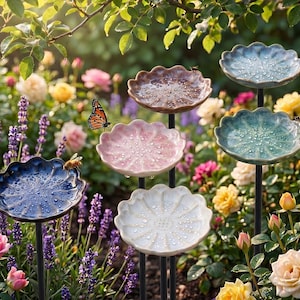 May include: A collection of six ceramic bird baths on thin black metal stakes, each featuring a scalloped, flower-shaped basin in various colours including blue, pink, brown, and white, with water droplets on the surfaces and a butterfly.