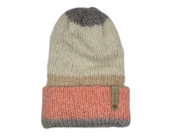 May include: A knitted beanie hat in a color-blocked design. The hat features a gray top, a cream-colored midsection, a tan band, and a coral pink brim. A small tag with the text "damnKnit" is attached to the brim.