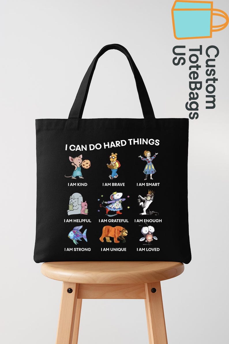 May include: Black tote bag with the text "I CAN DO HARD THINGS" and illustrations of various characters with positive affirmations like "I AM KIND" and "I AM BRAVE". The bag has black handles.