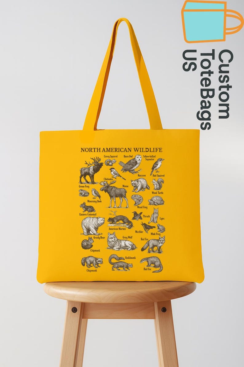 May include: A mustard yellow tote bag displaying a detailed illustration of North American wildlife. The bag features various animals and birds, with the text "NORTH AMERICAN WILDLIFE". The bag also has the text "Custom ToteBags US".