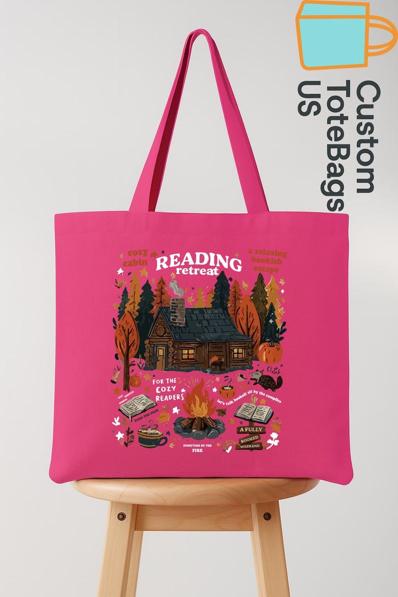 May include: A vibrant pink tote bag with a cabin scene and the words "READING retreat". The design includes a cabin, a campfire, books, and the text "For the Cozy Readers". The bag has long handles.
