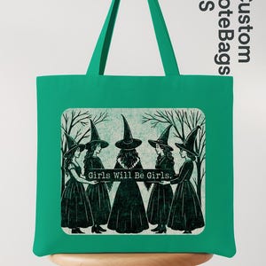 May include: A green tote bag with a rectangular graphic featuring five women in witch hats and dresses, holding hands. The text "Girls Will Be Girls" is below the image. The bag has a matching green handle.