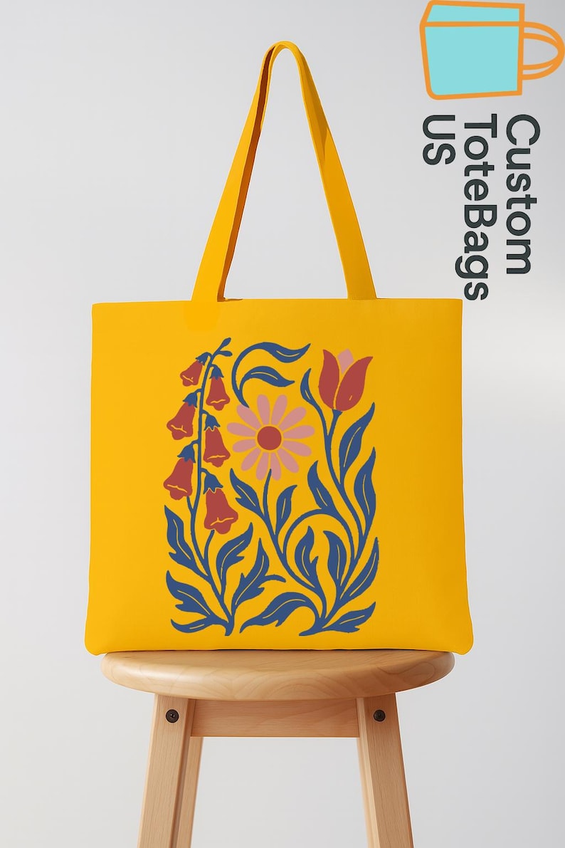 Peut inclure: Un sac fourre-tout jaune avec un motif floral. Le sac pr&eacute;sente un motif stylis&eacute; de fleurs et de feuilles en bleu, rose et rouge. Le sac est pos&eacute; sur un tabouret en bois. Le texte "Custom Tote Bags US" est visible.