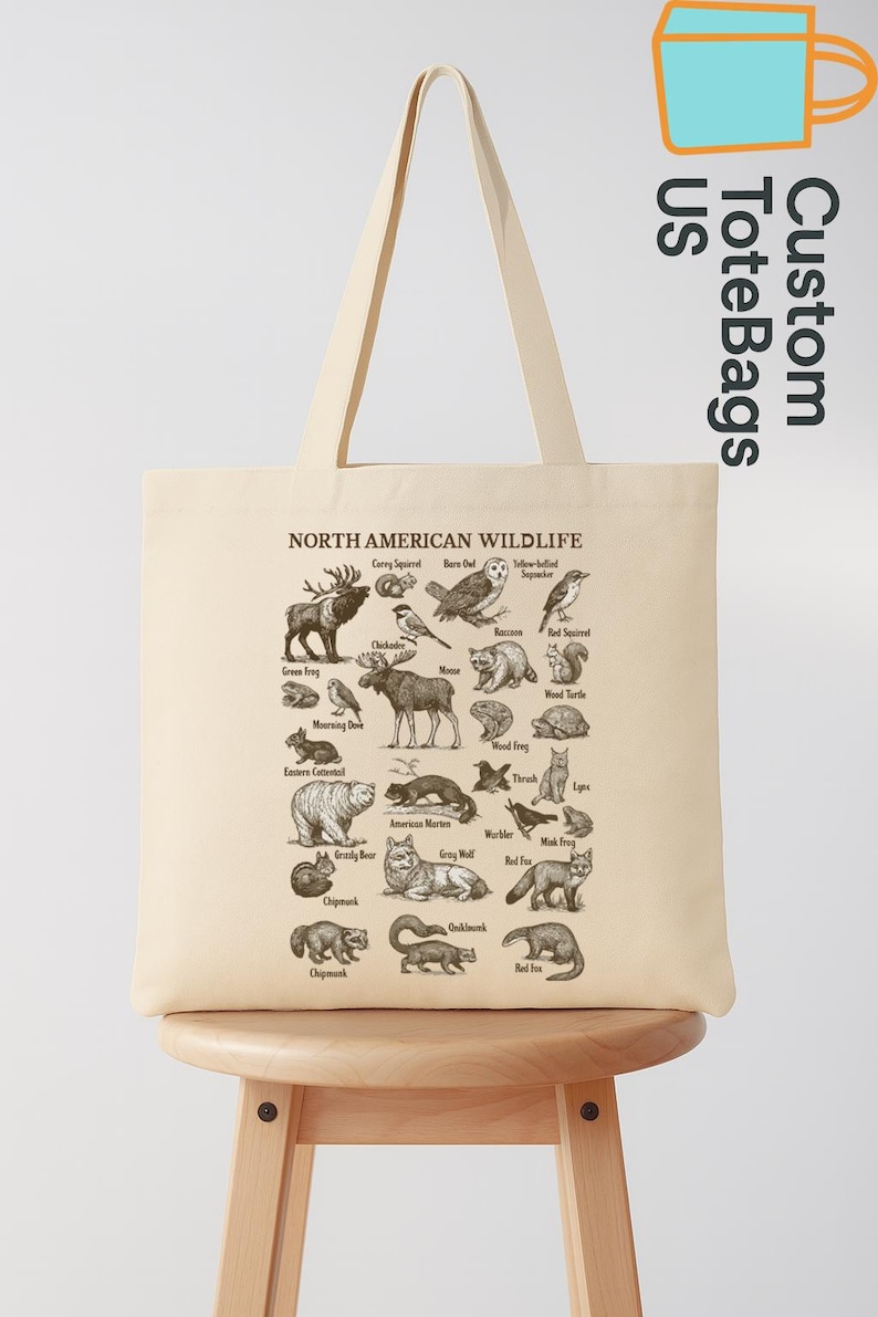 May include: A cream-coloured tote bag displaying a detailed illustration of North American wildlife, including animals such as bears, owls, and foxes. The bag features the text "NORTH AMERICAN WILDLIFE" and "Custom ToteBags US".