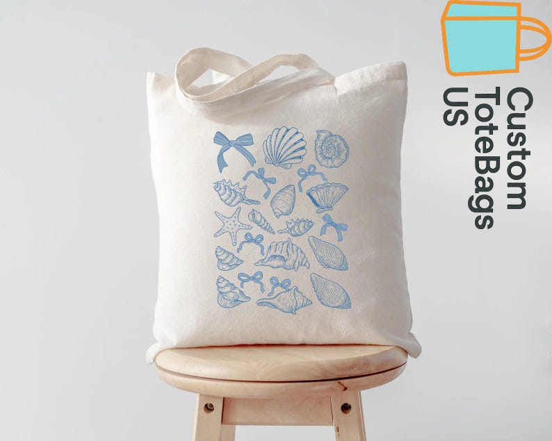 K&ouml;nnte beinhalten: Eine cremefarbene Tragetasche mit einem blauen Muschel- und Schleifenmuster. Die Tasche hat eine rechteckige Form und zwei Henkel. Der Text "Custom ToteBags US" ist auf der Seite aufgedruckt.
