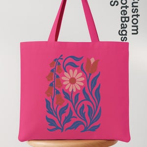 Peut inclure: Un sac fourre-tout rose vif avec un motif floral. Le motif pr&eacute;sente une marguerite, des fleurs en forme de cloche et des feuilles dans des tons orange, bleu et rose. Le sac a de longues anses roses et le texte "Custom Tote Bags US".