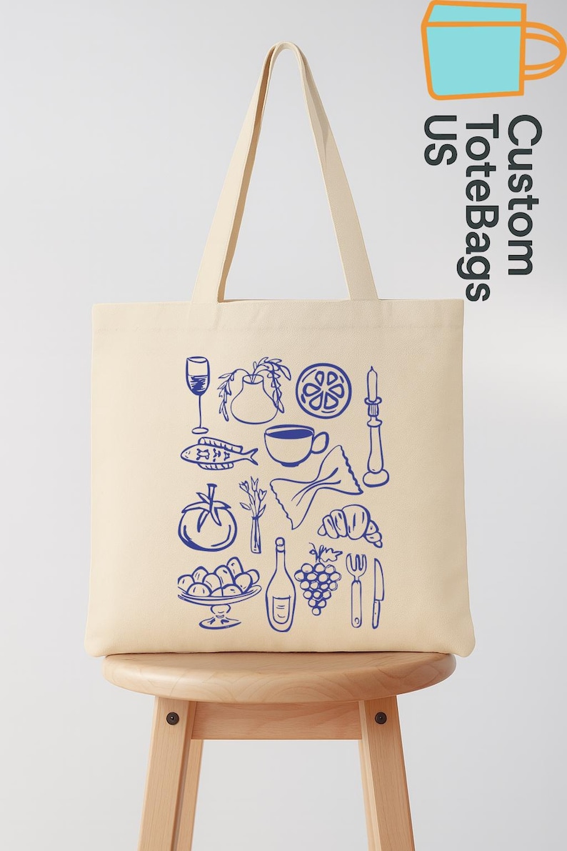 May include: Cream-colored tote bag with a blue line drawing of various food items, including a wine glass, fish, and grapes. The bag has long handles and the text "Custom Tote Bags US" in blue.