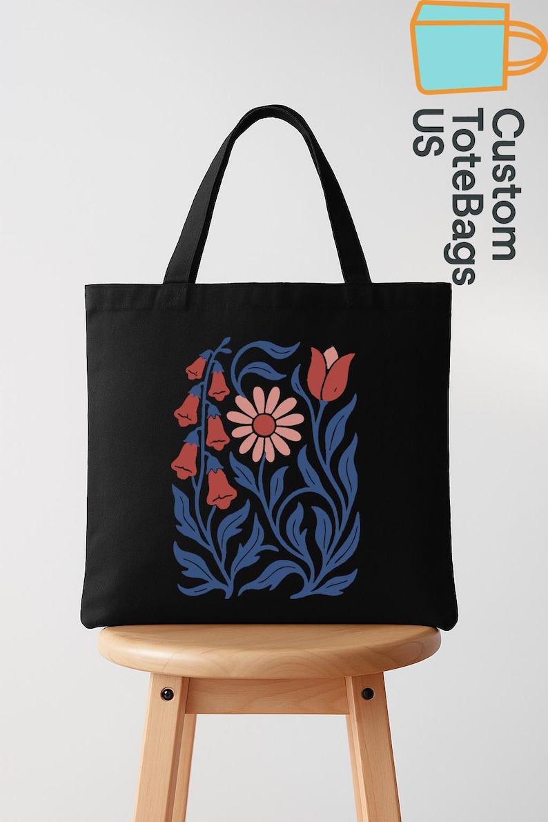 Peut inclure: Sac fourre-tout noir avec un motif floral de fleurs en clochettes rouges, une marguerite rose et des feuilles bleues. Le sac a des anses noires et est pos&eacute; sur un tabouret en bois. Le texte "Custom ToteBags US" est imprim&eacute; sur le c&ocirc;t&eacute;.