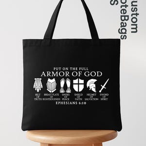 May include: Black tote bag with white text and illustrations. The text reads "PUT ON THE FULL ARMOR OF GOD" with depictions of a belt, breastplate, shoes, shield, helmet, and sword. The text "EPHESIANS 6:10" is also included.