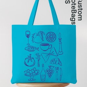 May include: A turquoise tote bag with a variety of food-related illustrations in blue. The bag features images of a wine glass, fish, tomato, pasta, croissant, and a bottle of wine. The text "Custom Tote Bags US" is printed on the side.