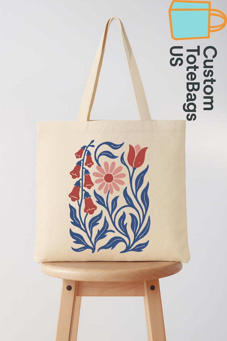 Peut inclure: Sac fourre-tout cr&egrave;me avec un motif floral de fleurs en clochettes rouges, une marguerite rose et des feuilles bleues. Le sac a de longues anses et le texte "Custom Tote Bags US".