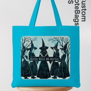 May include: A turquoise tote bag with a graphic of five women in witch hats and dresses, with the text "Girls Will Be Girls." The bag has a rectangular design and a turquoise handle.