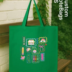 May include: A green tote bag featuring school-themed illustrations such as a bus, rainbow, and crayons. The bag has the text "BE KIND" and "Custom ToteBags US".