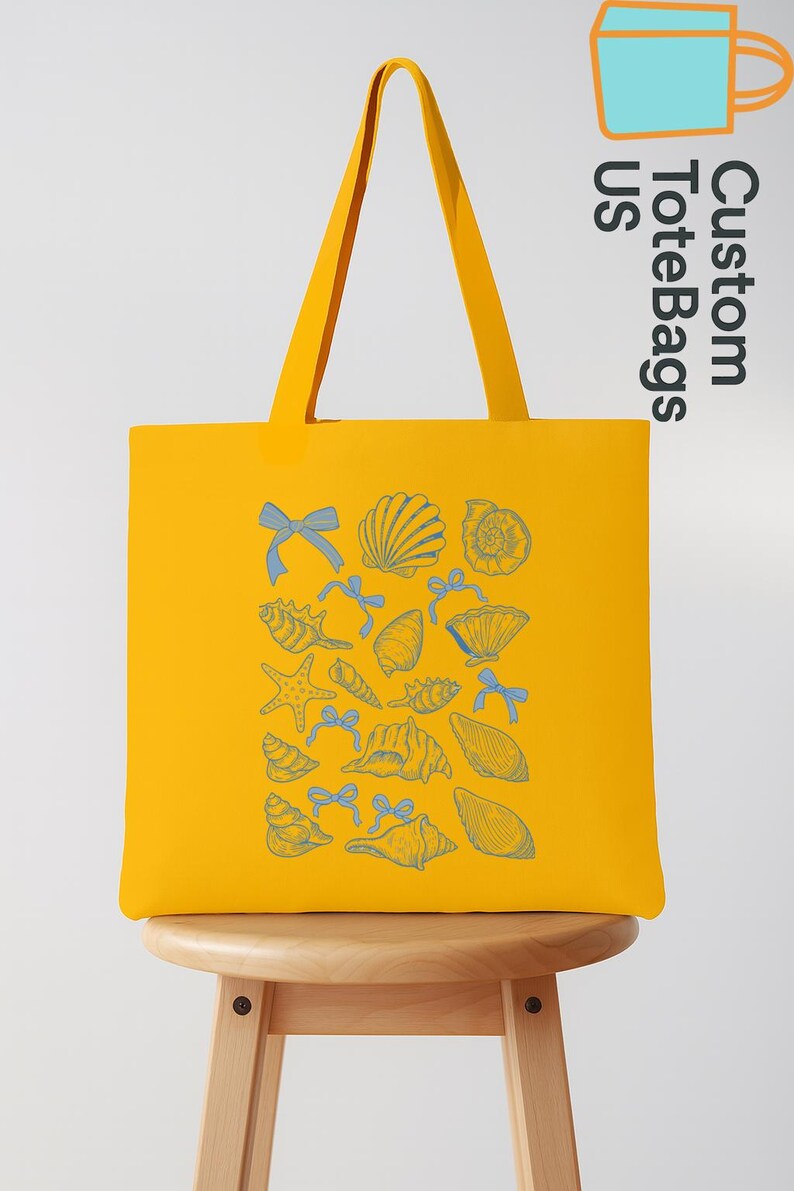 K&ouml;nnte beinhalten: Gelbe Tragetasche mit blauem Muschel- und Schleifenmuster. Die Tasche hat lange Henkel und steht auf einem Holzschemel. Der Text "Custom Tote Bags US" ist auf der Seite aufgedruckt.