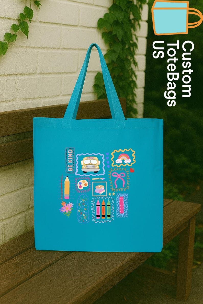 May include: A turquoise tote bag with school-themed illustrations, including a school bus, rainbow, pencil, and crayons. The text "BE KIND" is printed vertically. The bag has matching turquoise handles.