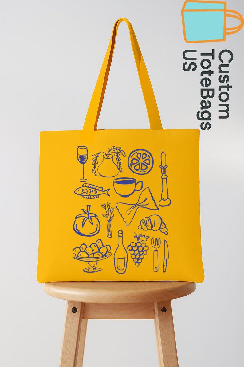 May include: Yellow tote bag with blue line art of food items like a wine glass, fish, tomato, and pasta. The bag has long handles and the text "Custom Tote Bags US" in the upper right corner.
