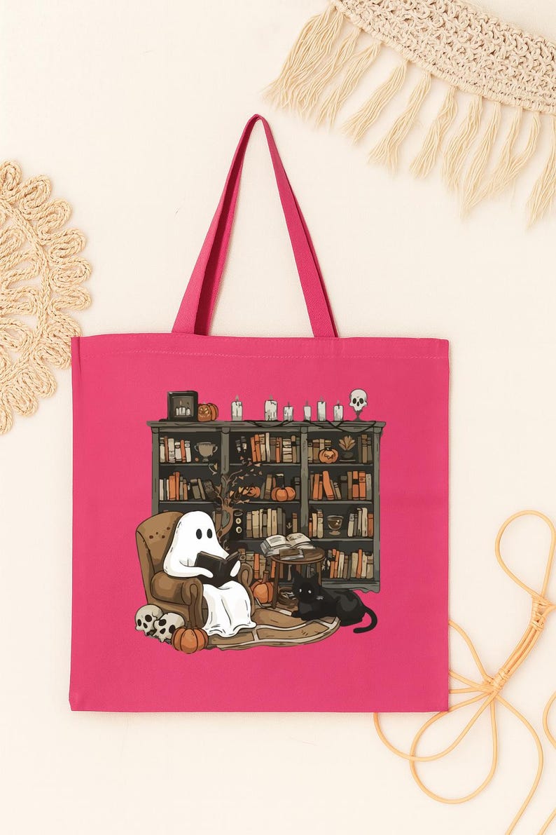 Puede incluir: Un bolso tote rosa intenso con una ilustraci&oacute;n de Halloween. Un fantasma lee en un sill&oacute;n frente a una estanter&iacute;a, con un gato negro cerca. Calabazas, velas y calaveras se suman a la escena espeluznante.