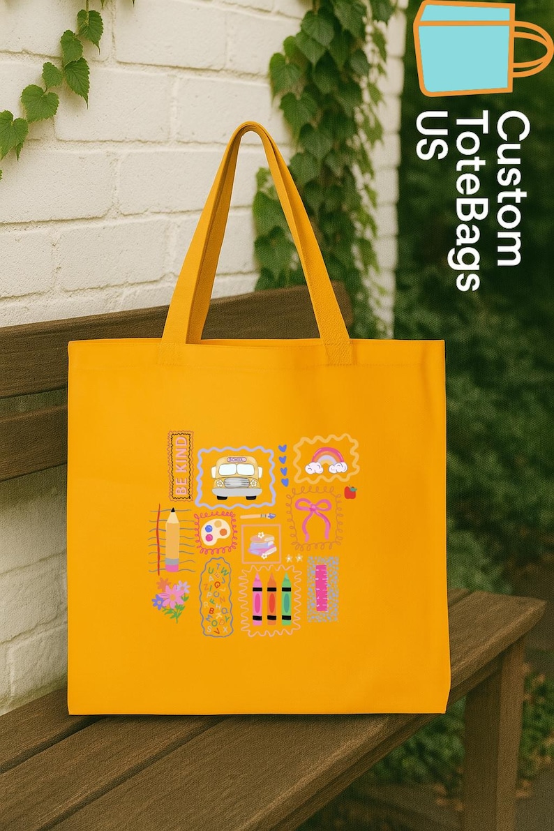 May include: A bright yellow tote bag featuring various colourful graphic designs, such as a school bus, rainbow, and pencils. The bag has long handles and the words "Custom ToteBags US" are printed on the side. The words "BE KIND" are also printed on the bag.