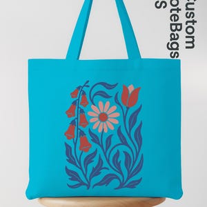 Peut inclure: Un sac fourre-tout turquoise avec un motif floral. Le motif pr&eacute;sente des fleurs rouges en forme de cloche, une marguerite rose et des feuilles et tiges bleues. Le sac a des anses turquoise assorties et le texte "Custom ToteBags US".