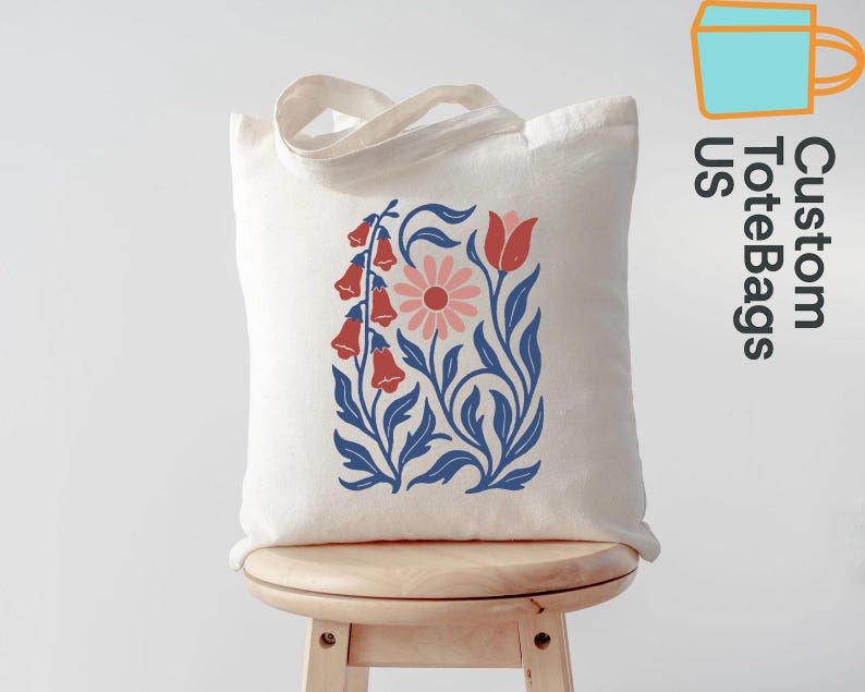 Peut inclure: Un sac fourre-tout cr&egrave;me avec un motif floral aux accents rouges, roses et bleus. Le motif comprend des fleurs en forme de cloche, une marguerite et des feuilles stylis&eacute;es. Le sac a une anse et le texte "Custom ToteBags US".