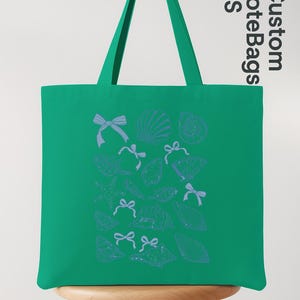 K&ouml;nnte beinhalten: Eine gr&uuml;ne Tragetasche mit blauen Muschel- und Schleifenillustrationen. Die Tasche hat eine rechteckige Form mit einem Griff. Die Worte "Custom Tote Bags US" sind auf der Seite aufgedruckt.