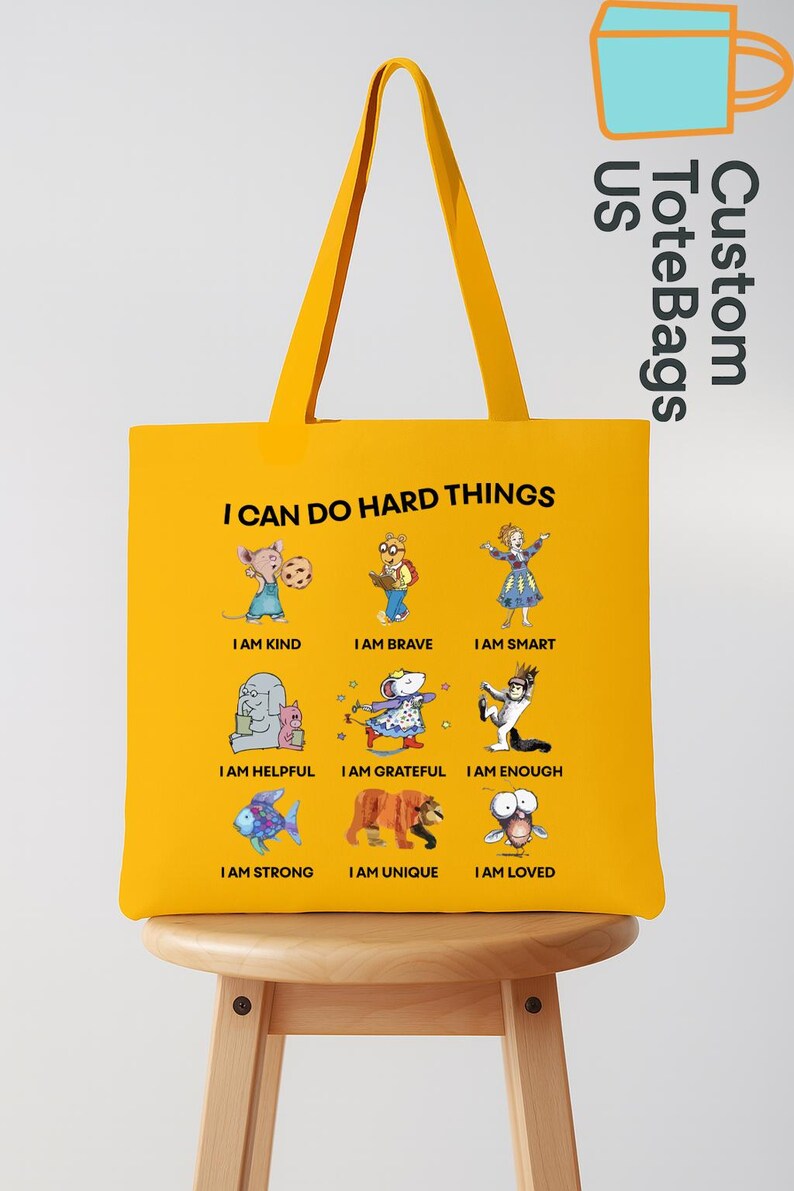 May include: Yellow tote bag with the text "I CAN DO HARD THINGS" and illustrations of cartoon animals with positive affirmations. The bag has a matching yellow handle and the words "Custom Tote Bags US" are printed on the side.