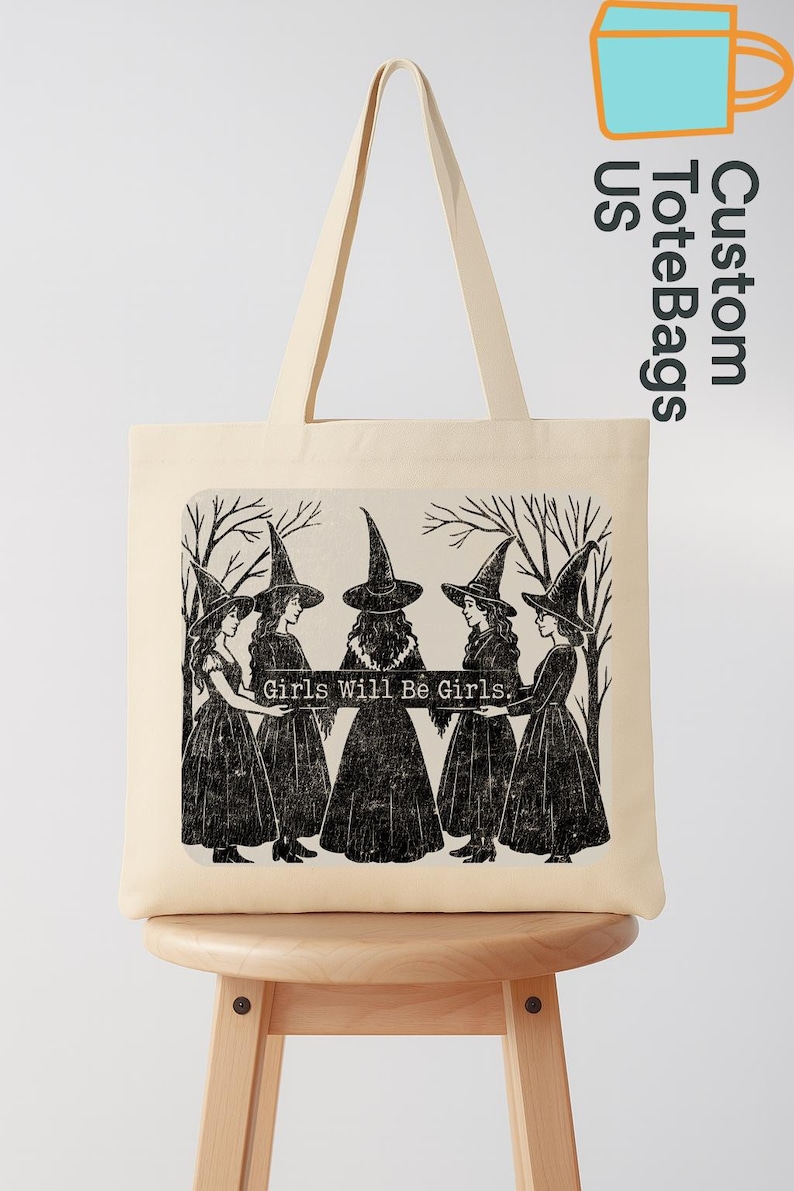 May include: A cream tote bag with a black and white illustration of five figures in witch hats and dresses, with the text "Girls Will Be Girls." The bag has long handles and a simple design.