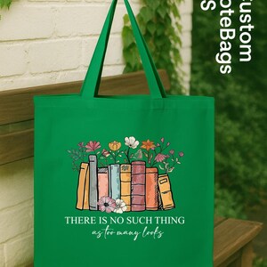 May include: Green tote bag featuring a colorful illustration of books with flowers. The bag has the text "THERE IS NO SUCH THING as too many books". The bag is made of a durable material and has long handles.
